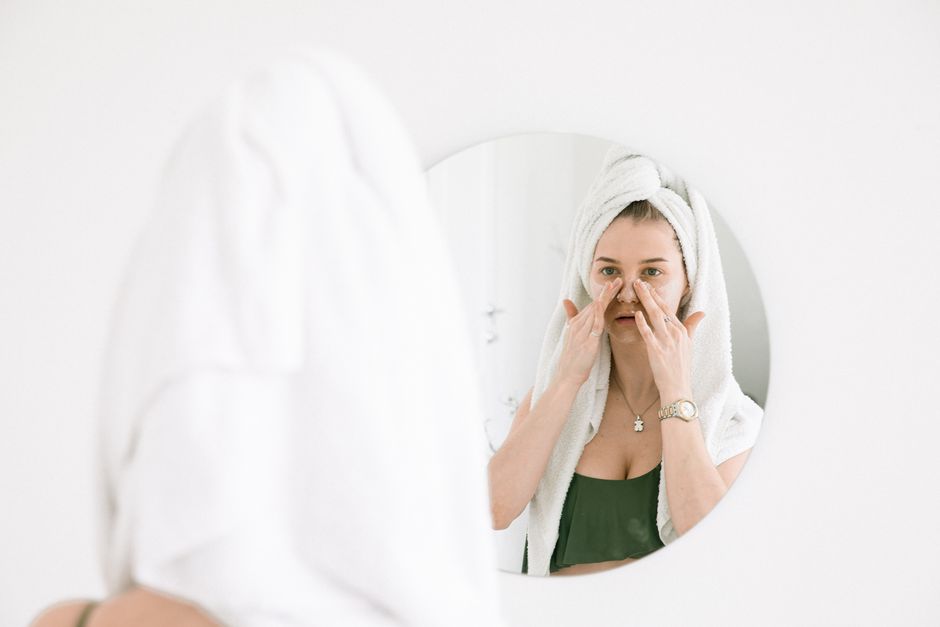Woman examining her skin in a mirror while considering cosmetic dermatology treatment options